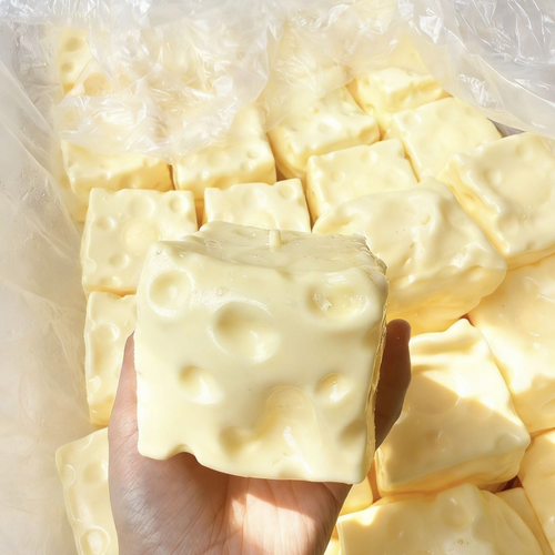 Pale yellow cheese-shaped squishy held in a hand, with additional cubes in the background